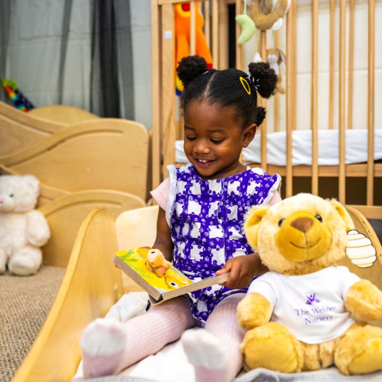 Nursery child reading a book with teddy bear